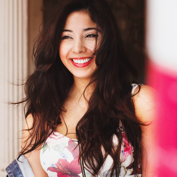 a person with long dark hair wearing a pretty flowered dress and a big smile